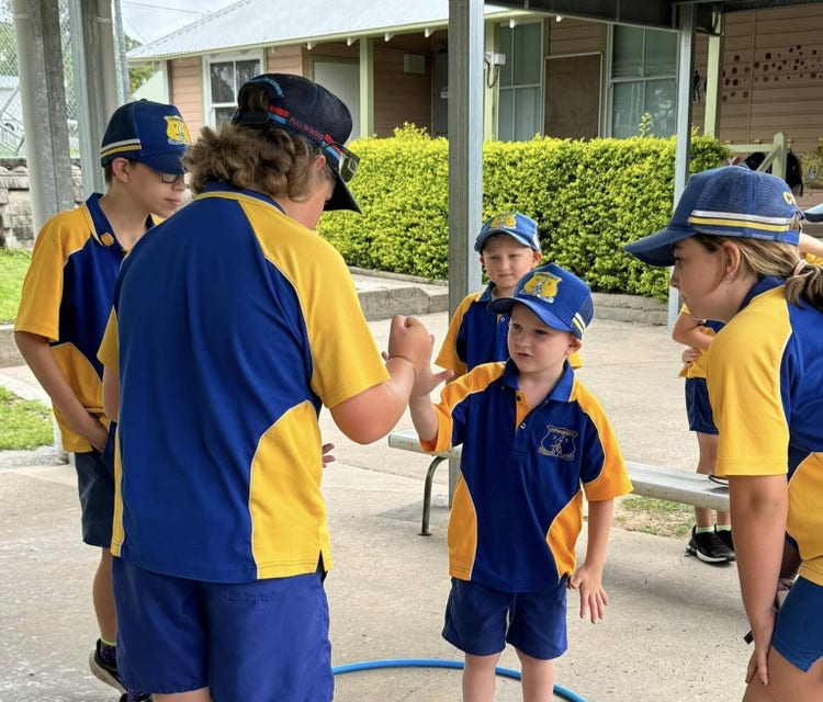photo of students in mixed sports groups all helping new kindergarten student with a game
